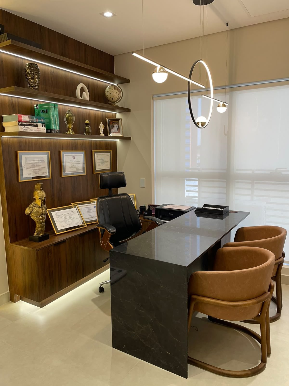 Consultório do Dr. Renan Bosio, com mesa de mármore e estante de diplomas