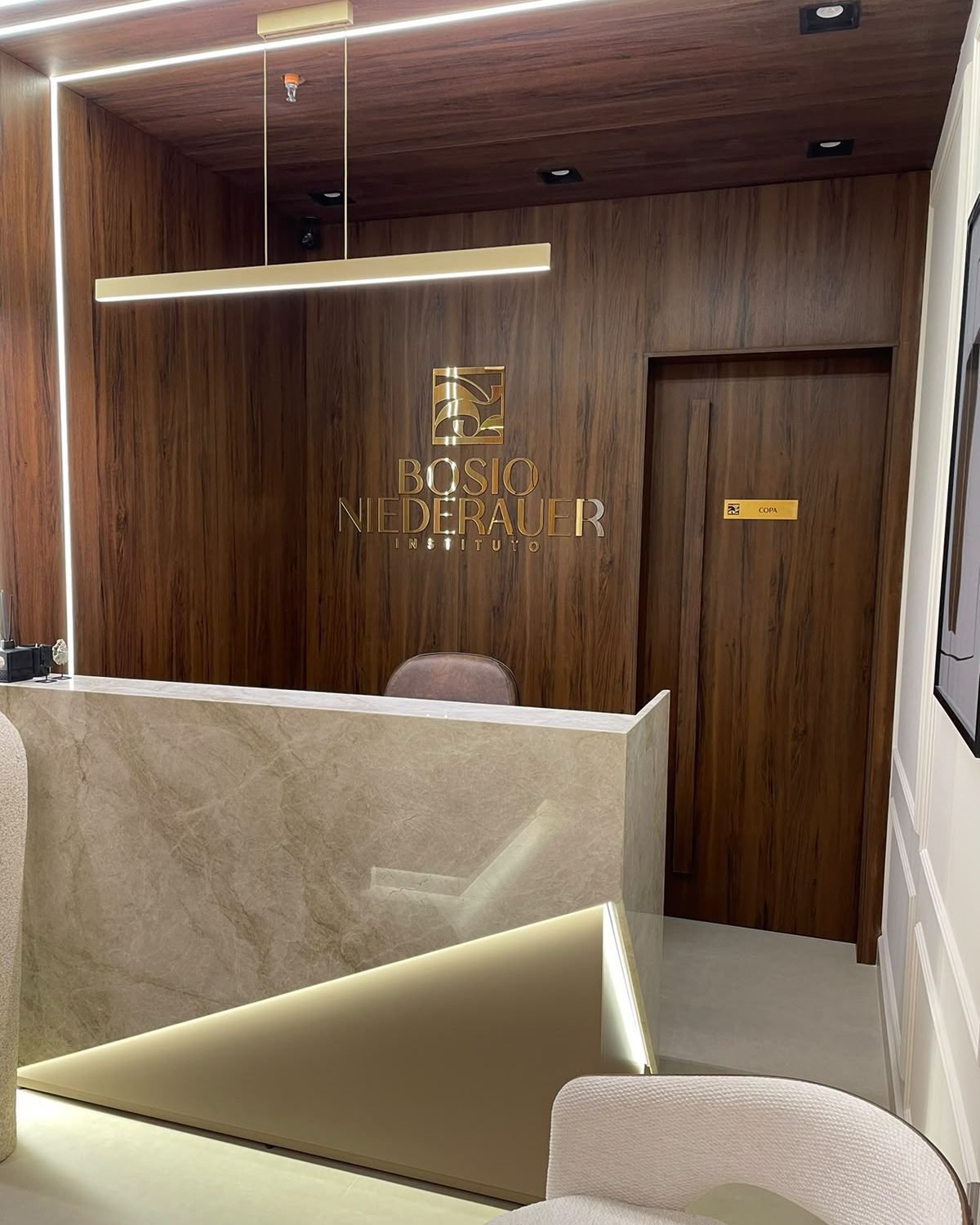 Recepção do Instituto Bosio Niederauer, com o logo dourado na parede de madeira